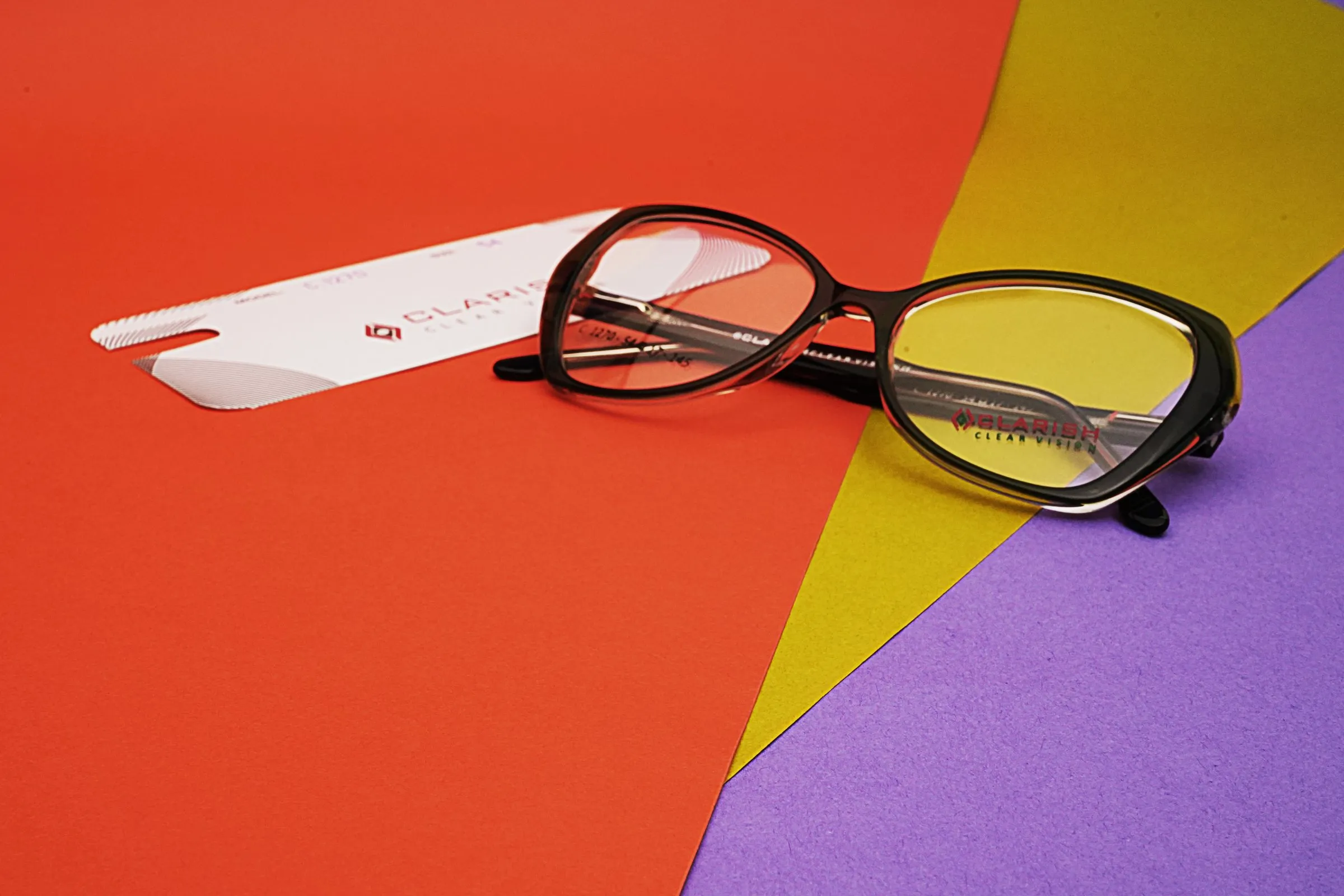A dark acetate optical frame photographed on layered coloured paper with a Clarish™ cleaning cloth