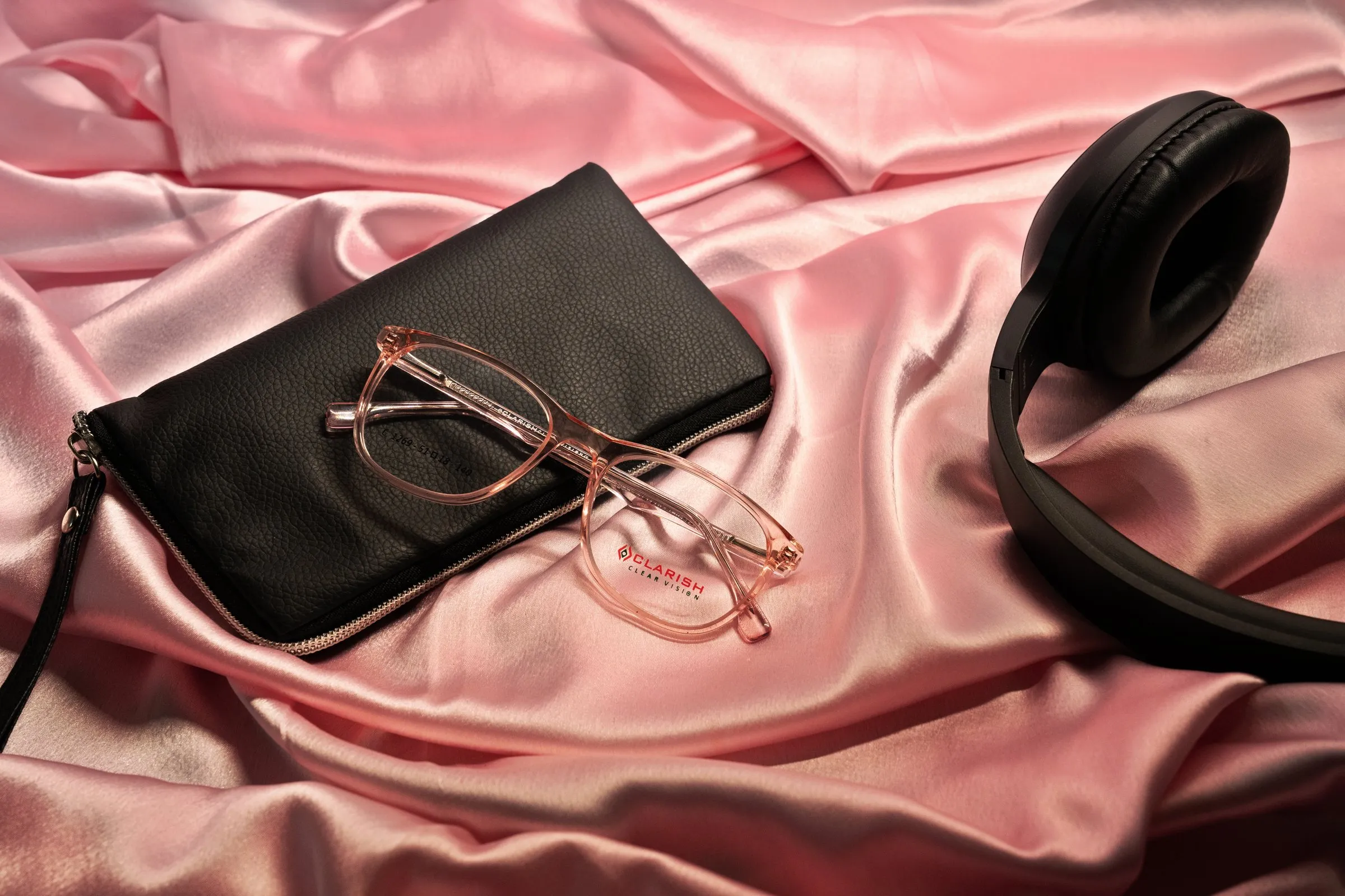A rose-toned Clarish™ frame styled on satin with a leather clutch